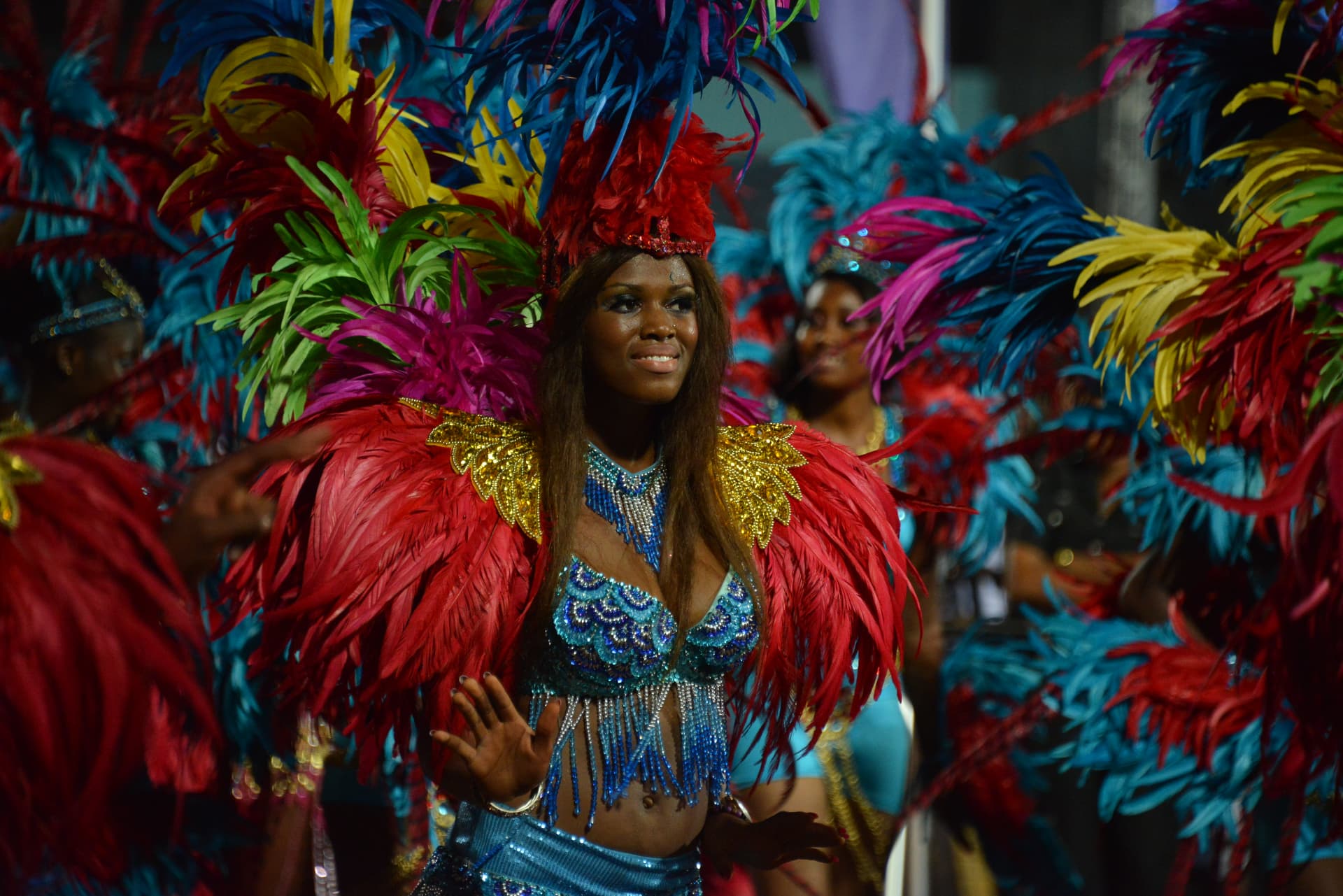 Carnival dancer in a red and blue feathered costume smiling on the route