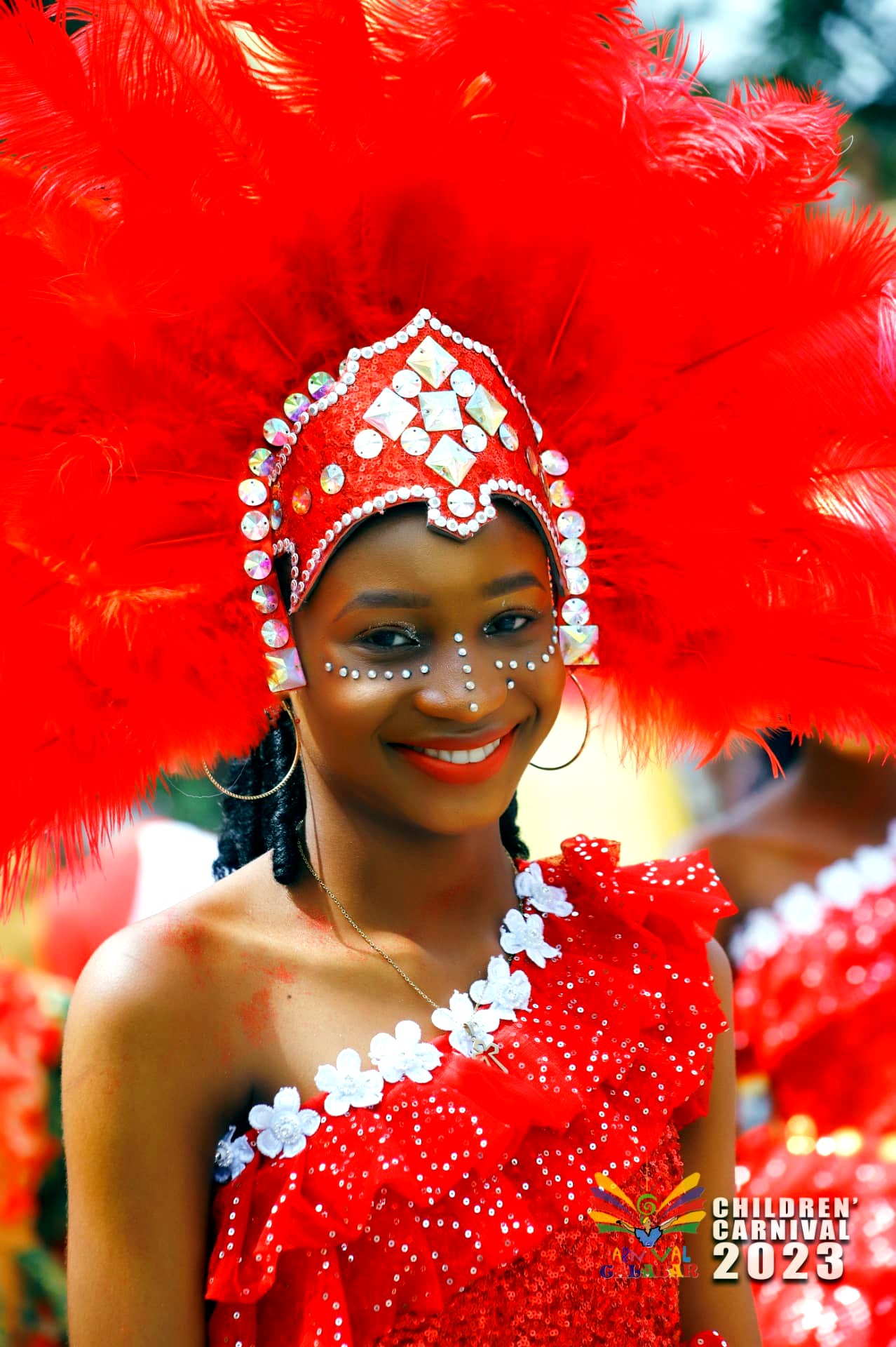 Young performer smiling in a towering crimson plume headdress