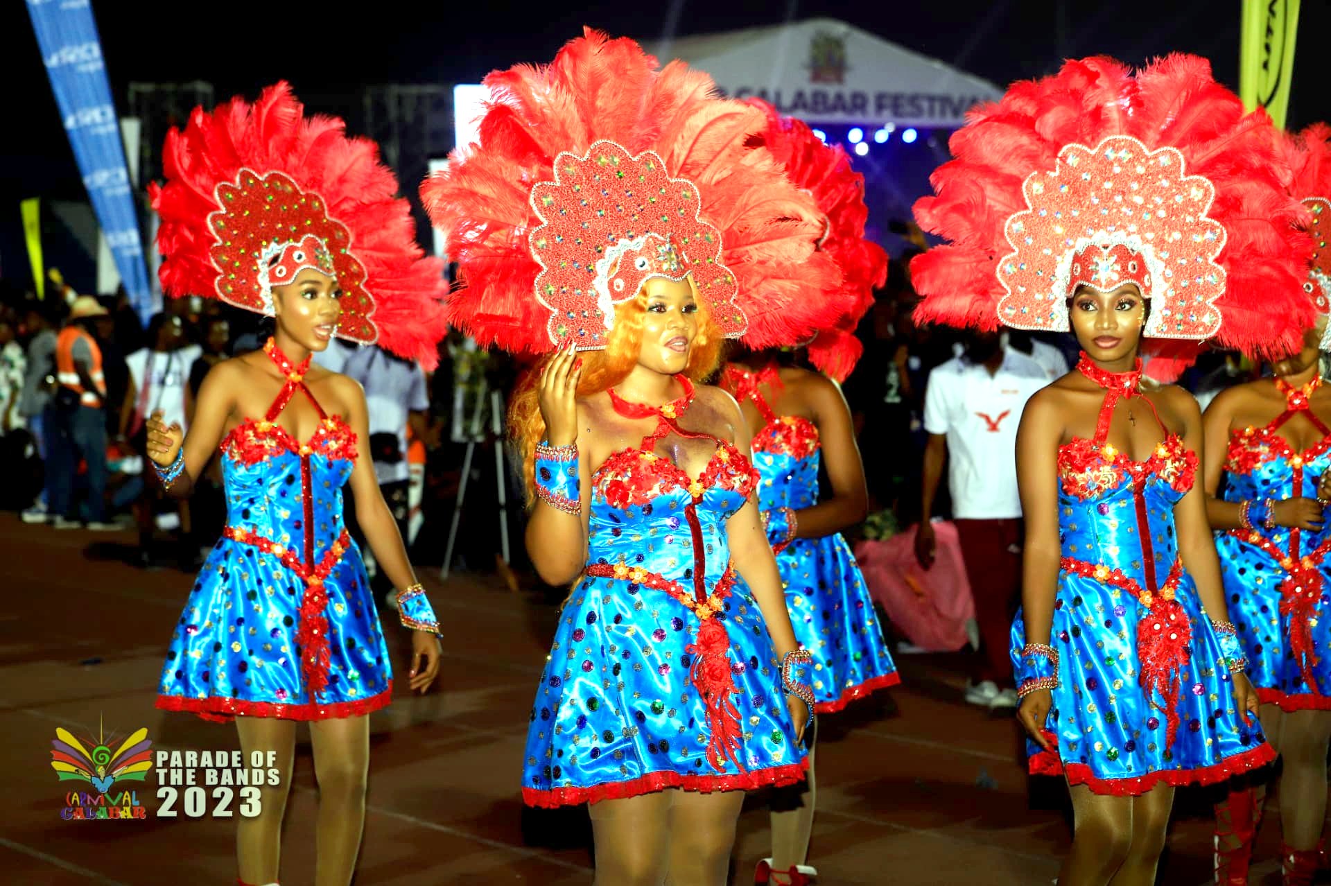 Three dancers in blue dresses and red feather headdresses at night